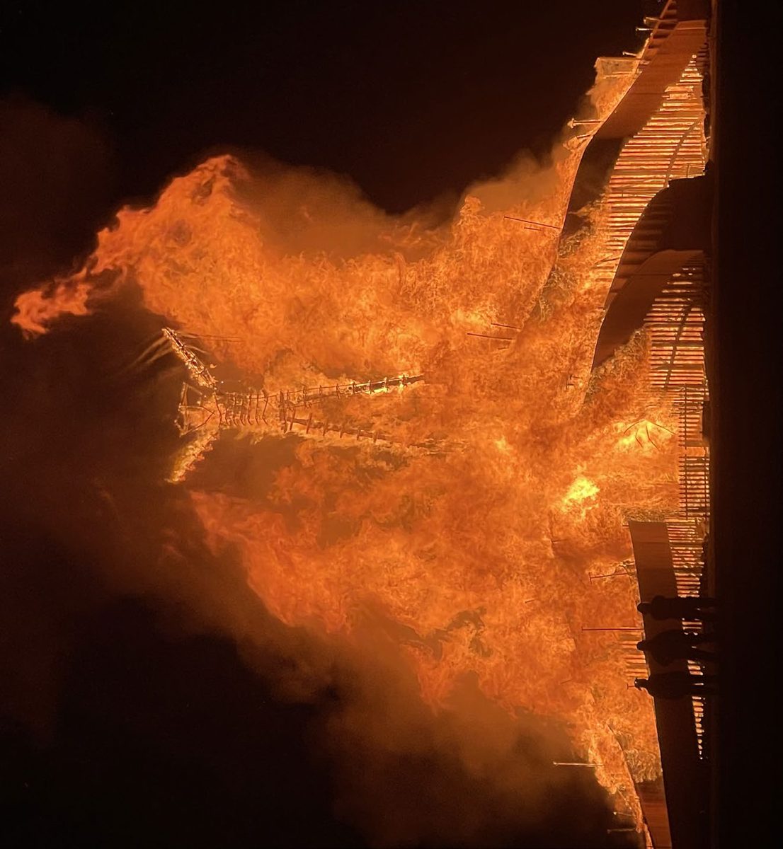 A figure of flame atop a burning pavilion at night.